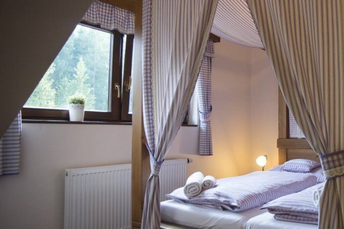 Un dormitorio con cama, mesitas de noche, una ventana con cortinas, un radiador y una pequeña planta en maceta.