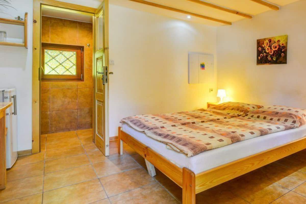Un dormitorio con una cama de madera, una mesita de noche, una lámpara, una puerta con ventanal y un cuadro colgado en la pared.