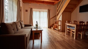 A cozy living room with a sofa, a coffee table, and a dining area with wooden chairs and a table. - Wellness Hotel Ondrášův Dvůr (Bílá)