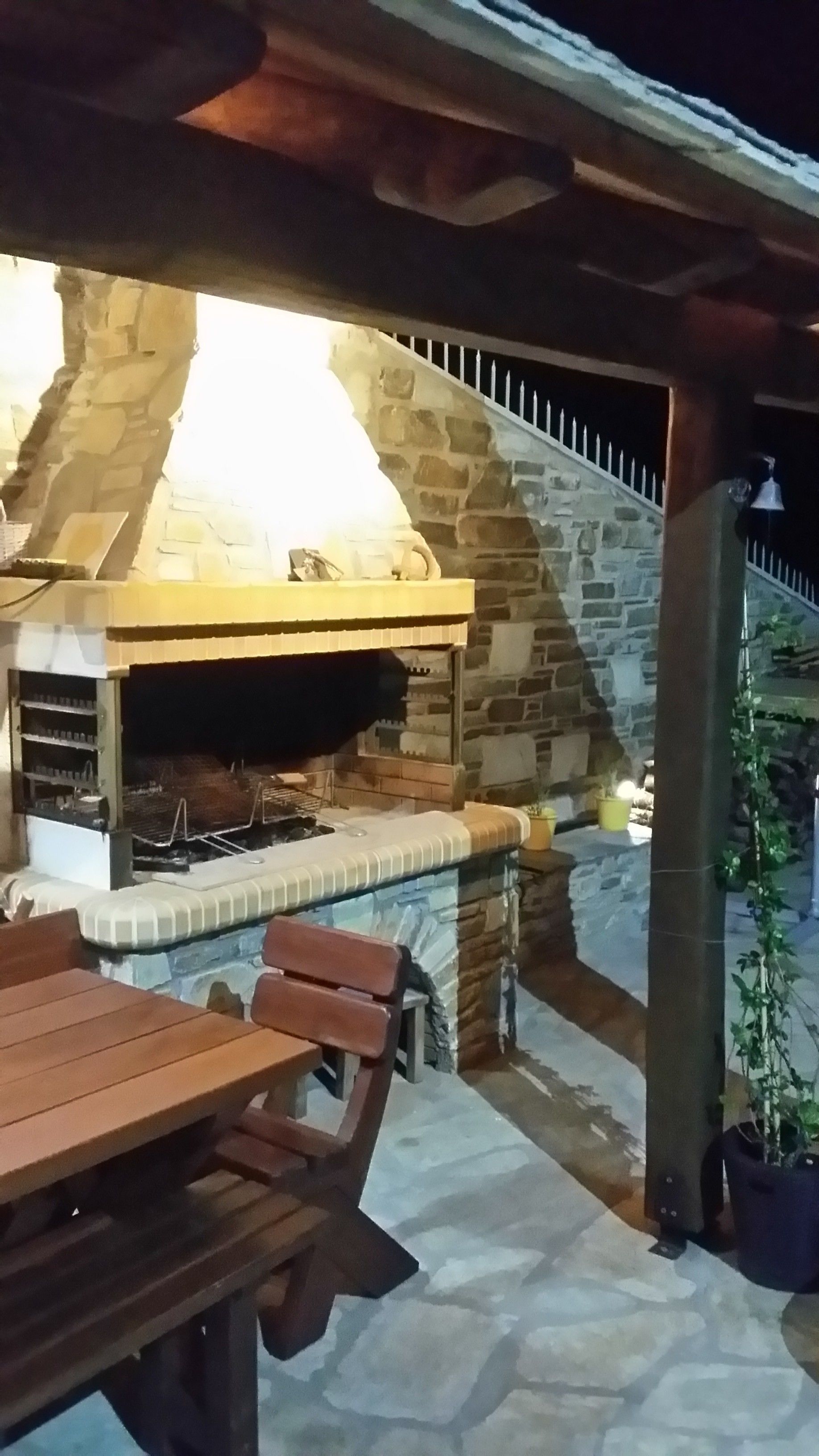 An outdoor stone barbecue area with a wooden table and benches.