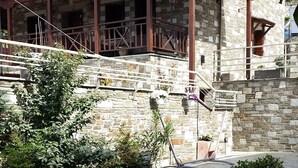 Edificio de piedra con balcón, rodeado de un jardín cuidado con plantas en macetas y un camino de piedra.