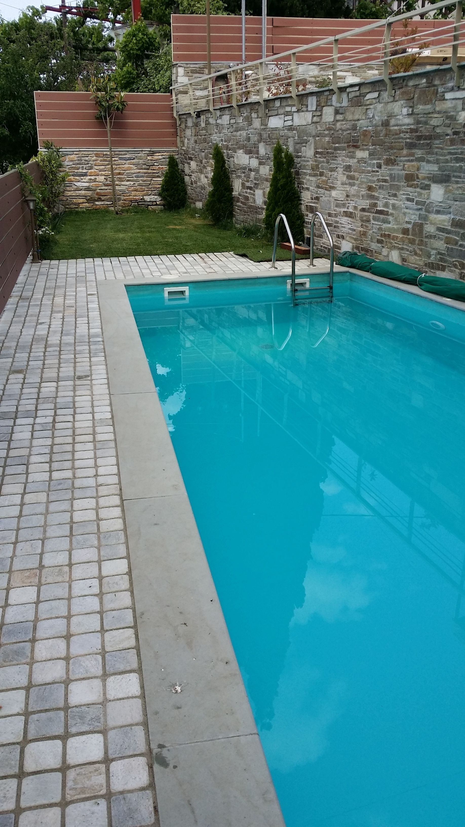 A swimming pool with a stone wall and a metal ladder.