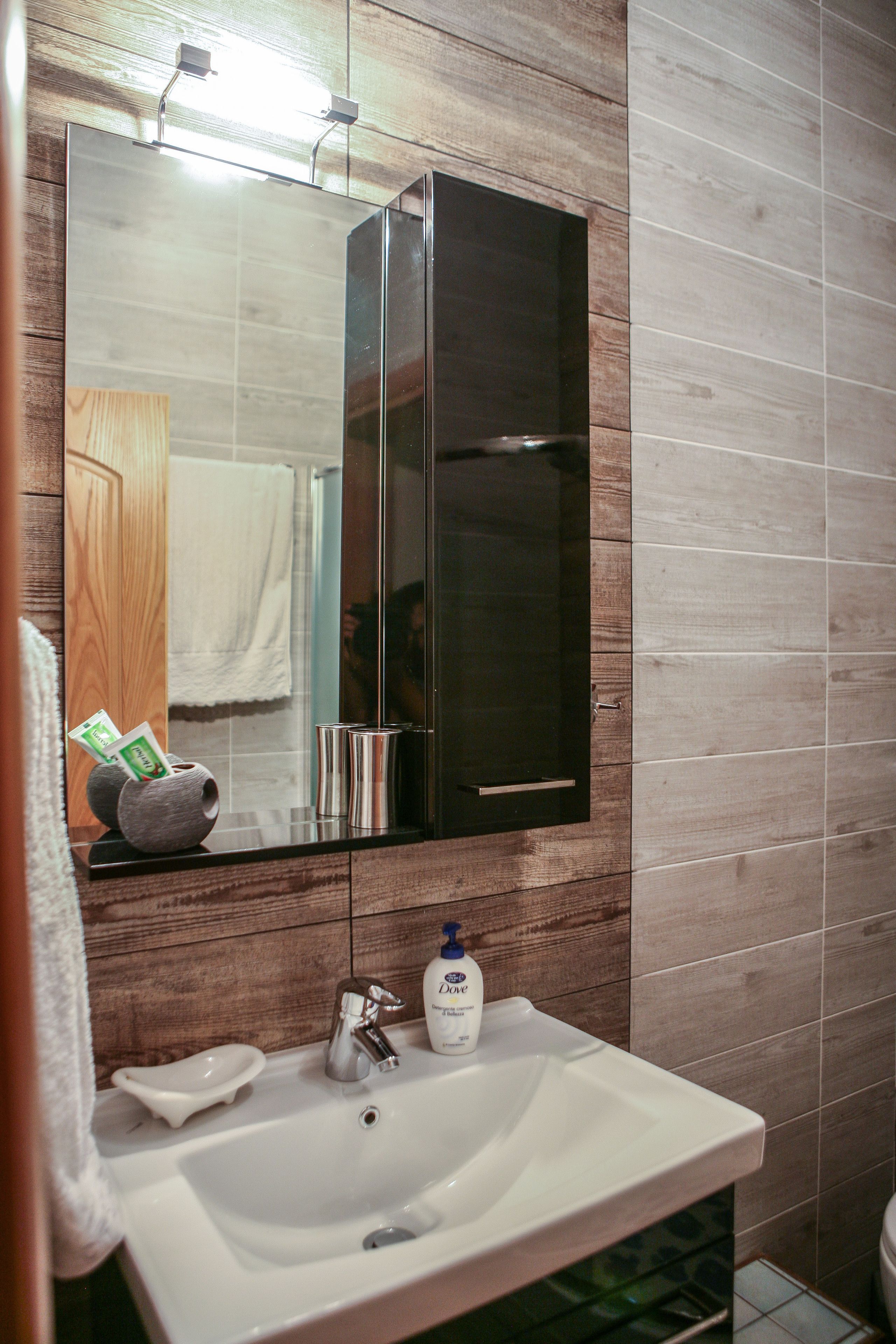 A bathroom with a large mirror, a white sink, and a wooden vanity.
