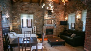 Una habitación acogedora con chimenea de piedra, una zona de comedor con mesa y sillas, un sofá y un televisor montado en la pared.