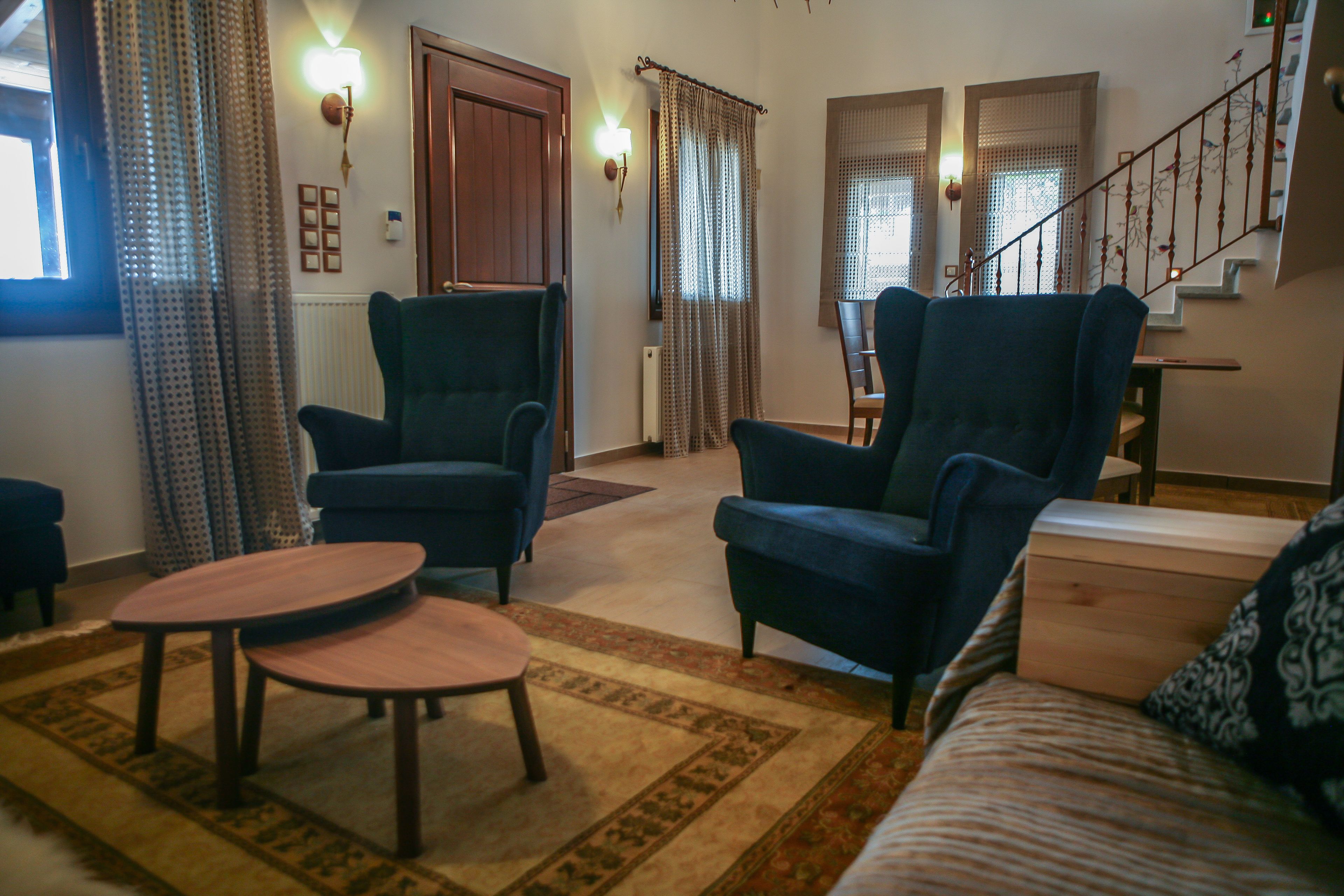 A living room with two armchairs, a coffee table, a sofa, a staircase, and a door with a light fixture.