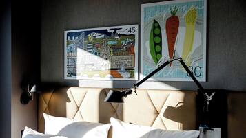 Una habitación de hotel con una cama, un cabecero, una lámpara de pared y dos cuadros enmarcados.