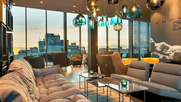 Un salon moderne doté d’une grande fenêtre, de sièges confortables et de luminaires suspendus.