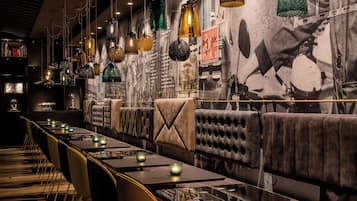 Ein Restaurant mit langen Tischen, gepolsterten Sitzecken und hängenden Pendelleuchten.