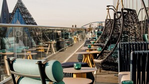 Une terrasse sur le toit, aménagée avec des espaces de détente en plein air, comprenant des chaises et des tables, et dotée d’une rambarde en verre.