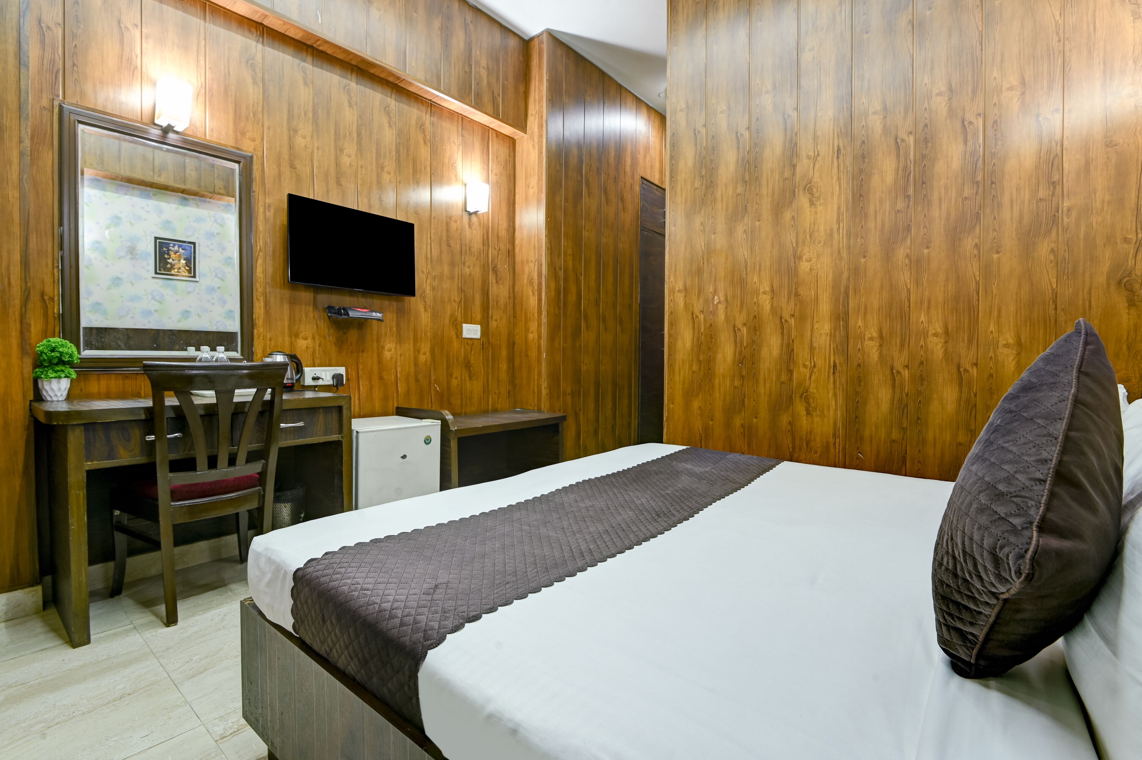 A room with a bed, a desk, a chair, a television, and a small refrigerator.