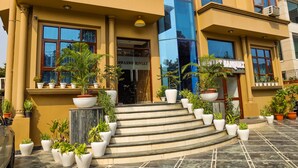 A hotel entrance with a modern facade, a staircase leading to the entrance, and potted plants around the steps. - Swasno By Rivlet (Gurugram)