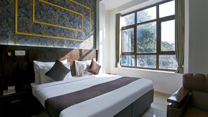 A neatly arranged hotel room with a large bed, a wooden headboard, a window with curtains, and a small seating area. - Swasno By Rivlet (Gurugram)