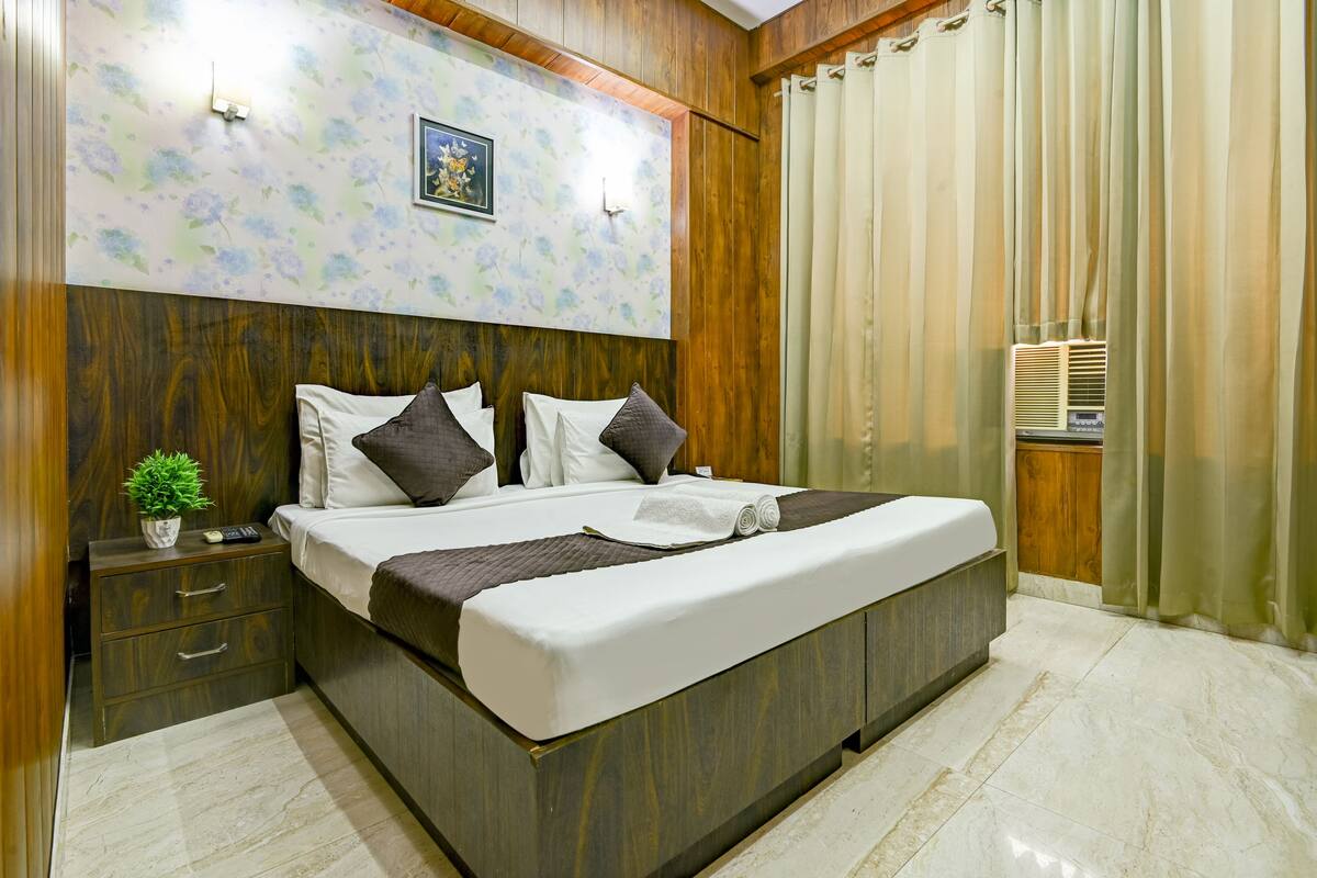 A neatly made bed with a headboard, a bedside table with a plant, and a wall-mounted light fixture.