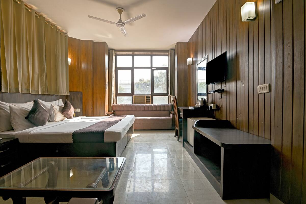 A hotel room with a bed, a sofa, a TV, a desk, and a window with curtains.