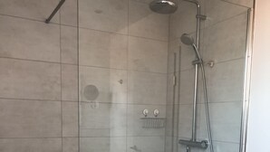 A glass-enclosed shower with a handheld showerhead and a fixed wall-mounted faucet.