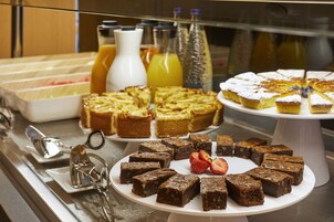 Egy svédasztal, amelyen különféle desszertek – köztük brownie-k és egy sütemény – és számos ital található.