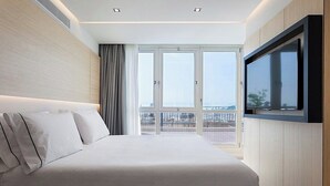 Habitación de hotel moderna con una cama grande, un televisor montado en la pared y un balcón con vistas.
