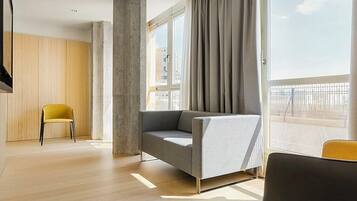 Una sala de estar moderna con un sofá gris, un sillón amarillo y un ventanal con cortinas.