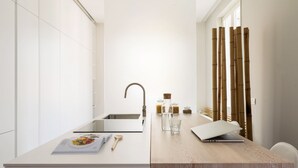 A modern kitchen with a white countertop, a stainless steel sink, and a wooden dining table. - Home at Hotel Boccherini luxury studio (Milan)