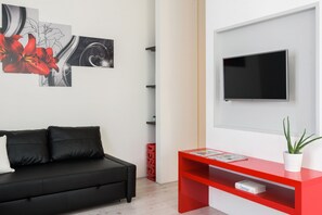 A modern living room with a black sofa, a red console table, and a flat-screen TV mounted on the wall.