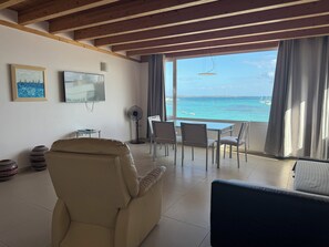 A living room with a view of the sea, a TV, and a fan.