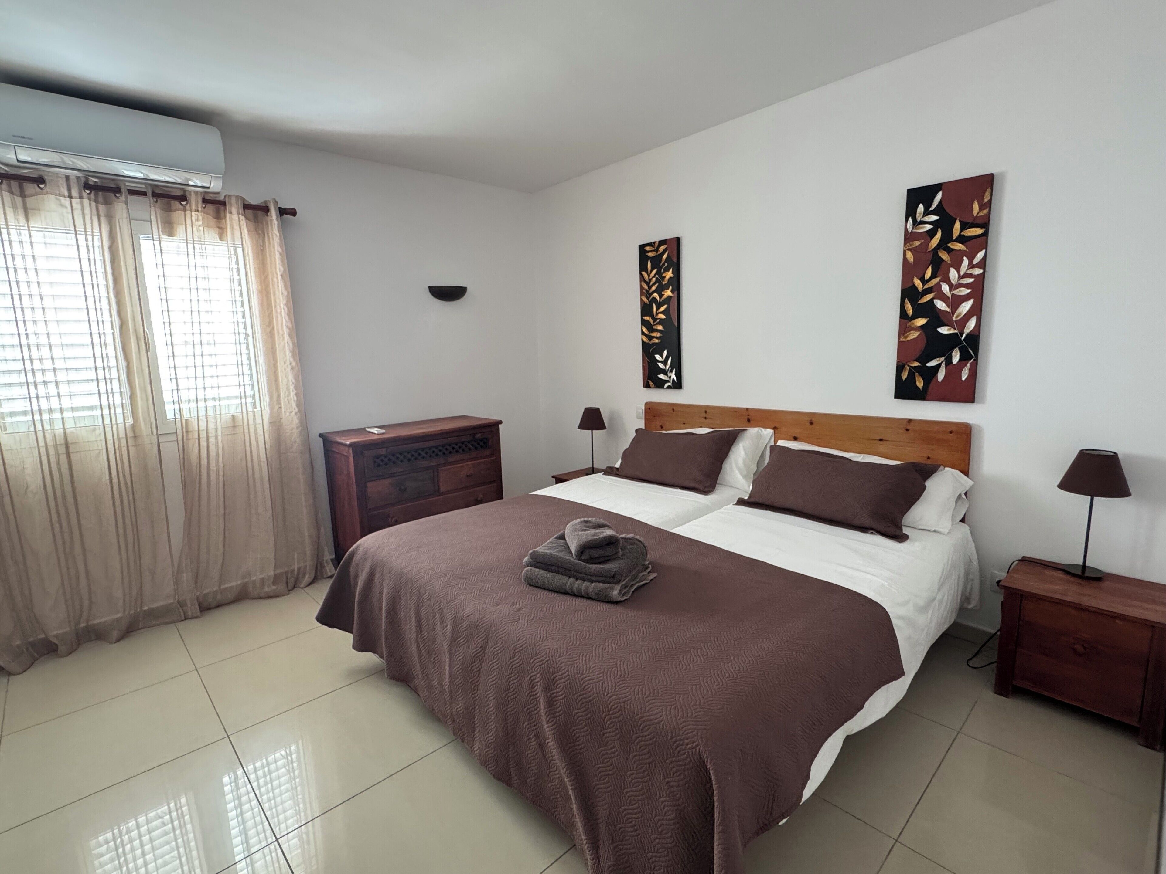 A bedroom with a large bed, two bedside tables, a dresser, and artwork on the walls.