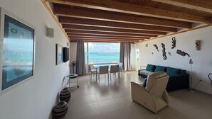 A spacious living area with a wooden ceiling, a sofa, a TV, and a view of the sea.