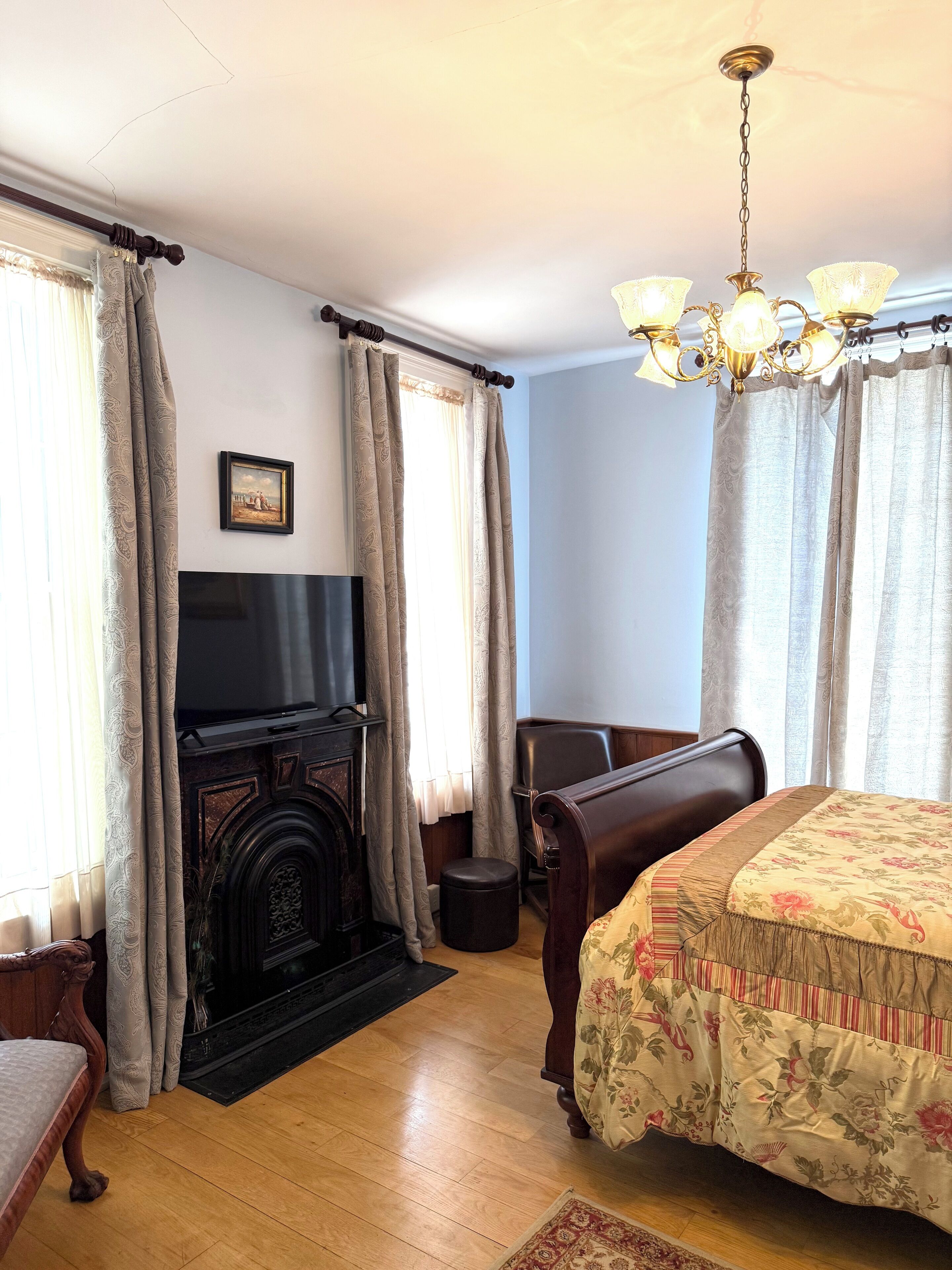 Una habitación con chimenea, cama con ropa de cama floral, piso de madera y candelabro.