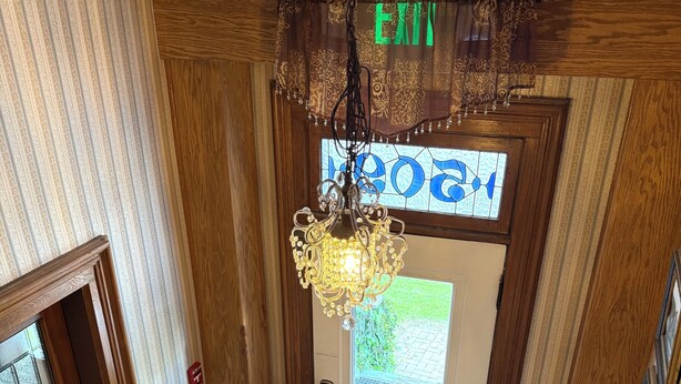 Interior de madera con escalera, candelabro y puerta con letrero que dice 'EXIT'.