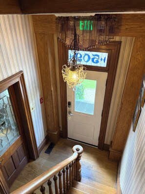 A wooden interior with a staircase, a chandelier, and a door with a 'EXIT' sign.