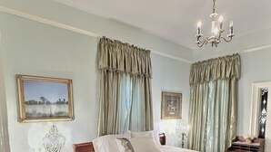 Un dormitorio con una cama grande, cabecera de madera, dos mesitas de noche, una araña y un cuadro enmarcado en la pared.