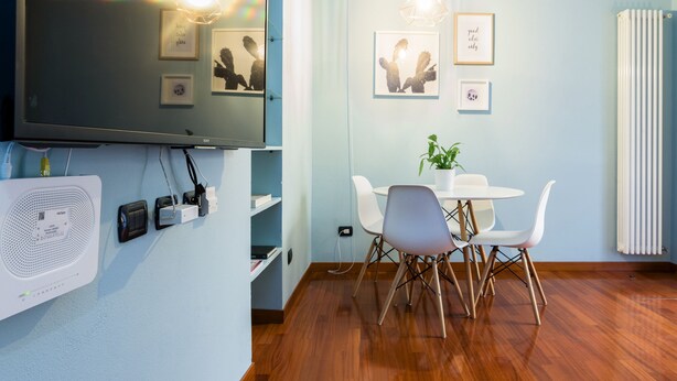A modern room with a large flat-screen TV, a white fan, and a dining area with a table and chairs. - Home at Hotel Naviglio - Sambuco Apt (Milan)