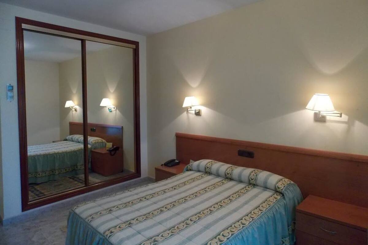 Une chambre d’hôtel comprenant un lit, une table de chevet, un miroir et deux lampes fixées au mur.