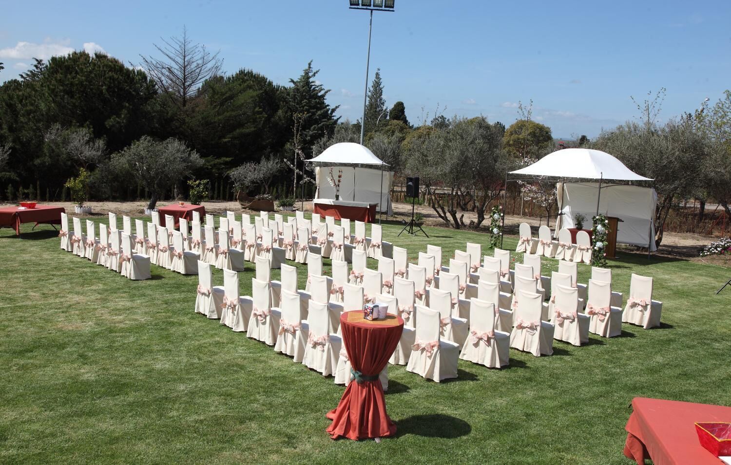Montaje para un evento al aire libre con filas de sillas y mesas, carpas y un escenario.