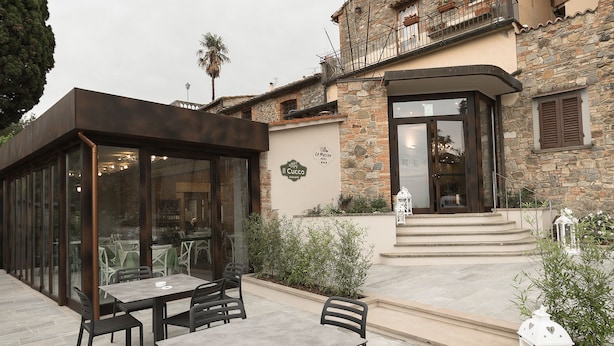 An outdoor patio with a table and chairs, a stone building with a balcony, and a sign that reads "Cucco". - Hotel le Macine (Montaione)