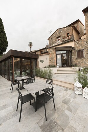 An outdoor patio with a table and chairs, a stone building with a balcony, and a sign that reads "Cucco". - Hotel le Macine (Montaione)