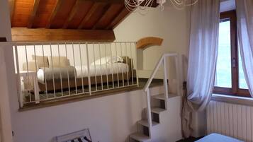 Une chambre à coucher avec un lit, un escalier, un lustre et une fenêtre avec des rideaux.