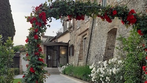 A stone building with a paved entrance and a decorative archway with red flowers. - Hotel le Macine (Montaione)