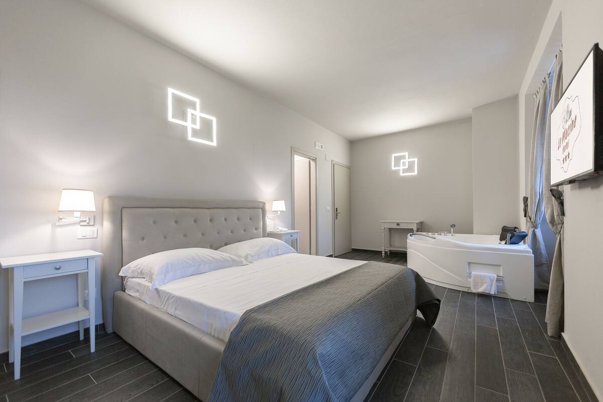 Ein modernes Hotelzimmer mit einem großen Bett, Nachttischen, einer integrierten Badewanne und einem kleinen Schreibtisch.