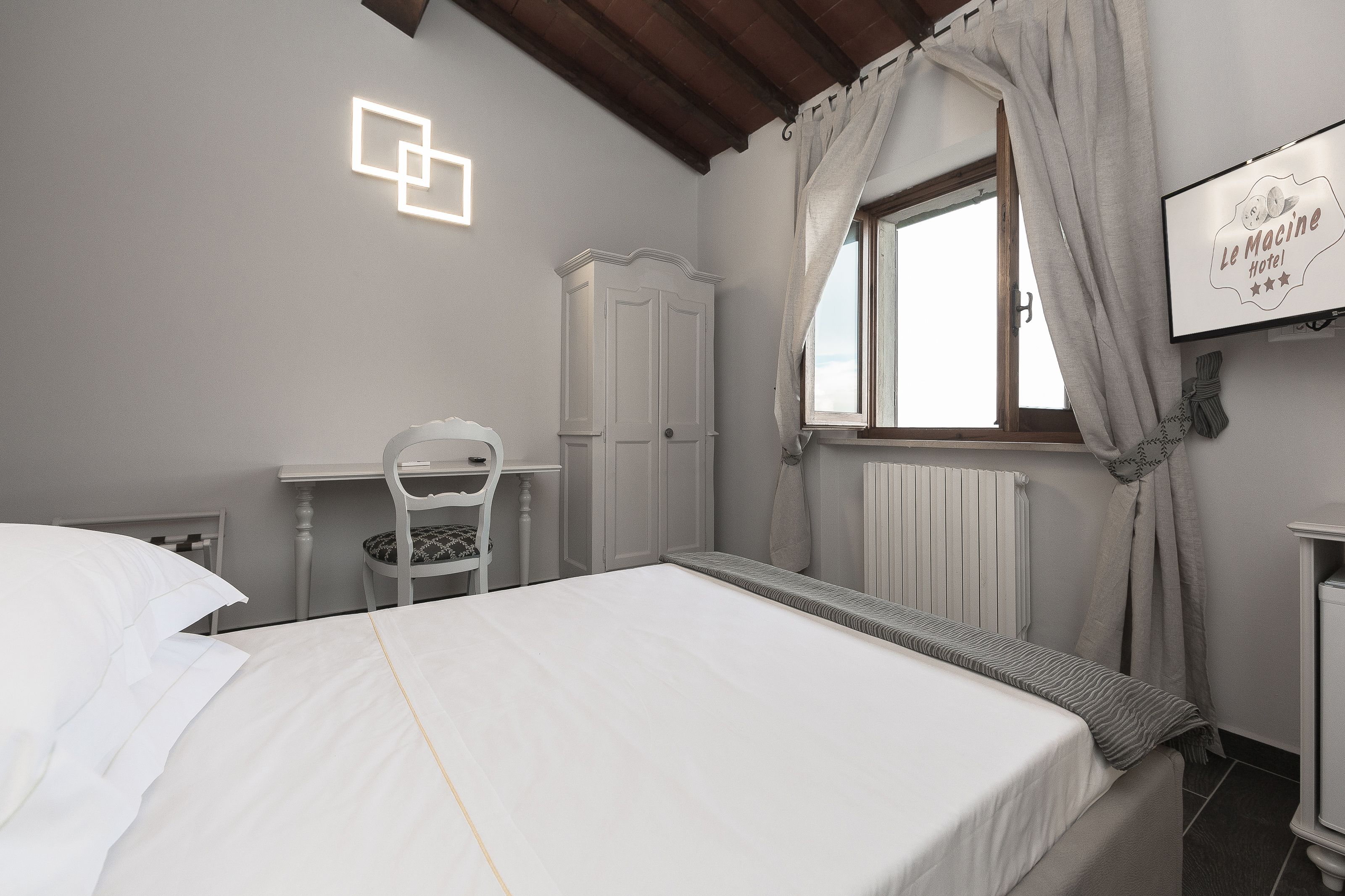 Un dormitorio con cama, una silla, armario y ventana con cortinas.