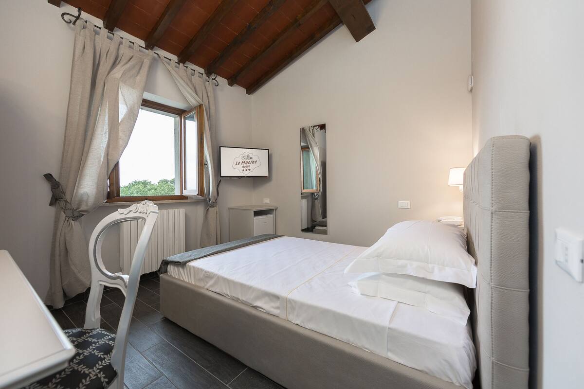 Ein Schlafzimmer mit Bett, Sessel, Nachttisch, Spiegel und einem Fenster mit Vorhängen.