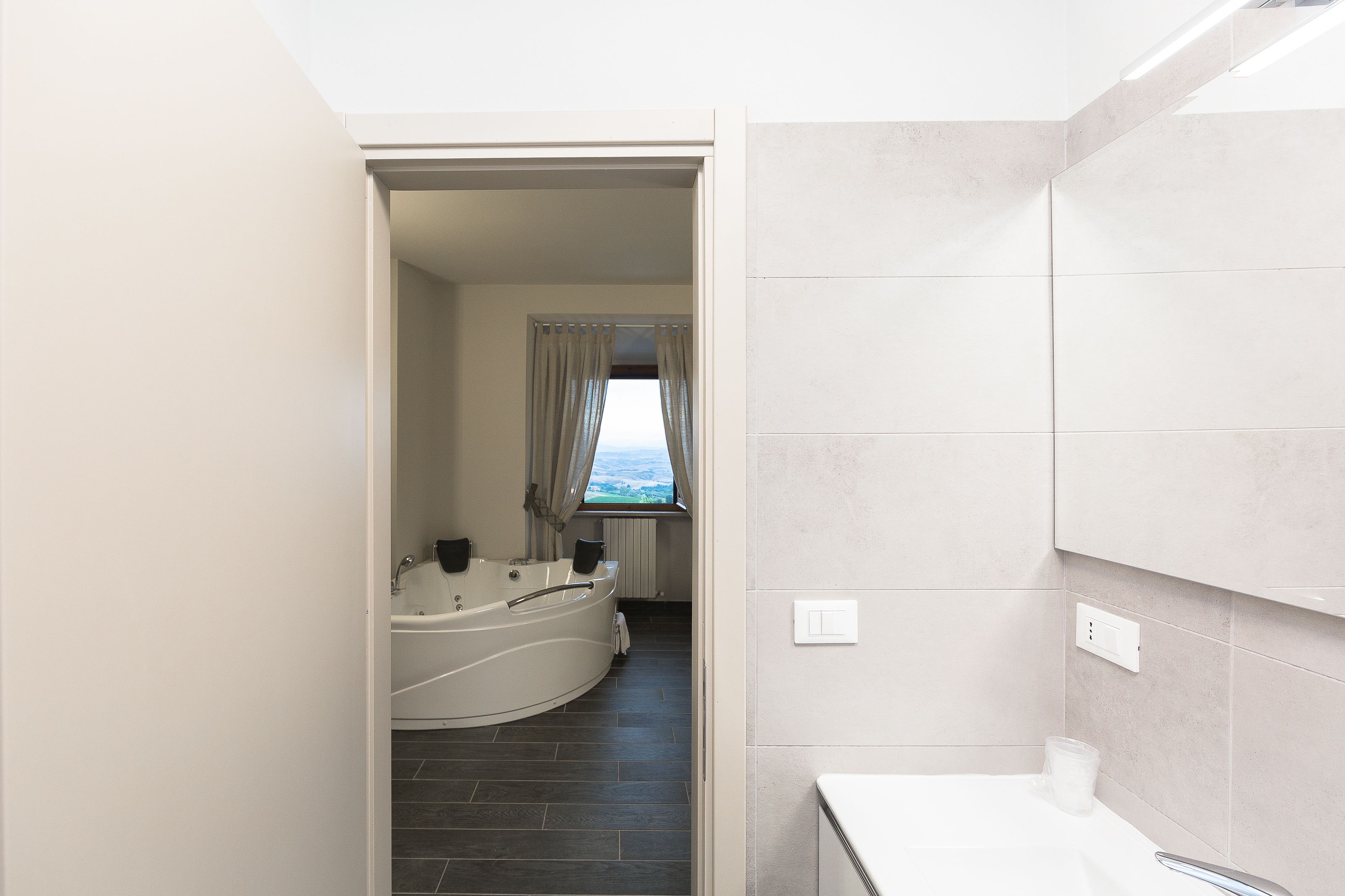 Ein modernes Badezimmer mit Badewanne, Duschbereich und einem fenster mit Vorhängen.