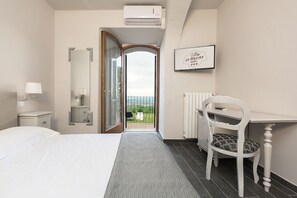 A hotel room with a bed, a desk, a chair, a radiator, and a view of the outdoors. - Hotel le Macine (Montaione)