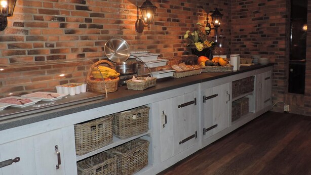 A buffet setup with a brick wall backdrop, baskets, and food items. - Hotel Ekamper (Roodeschool)