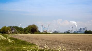 A rural landscape with wind turbines, a construction crane, and a building with smoke emissions.