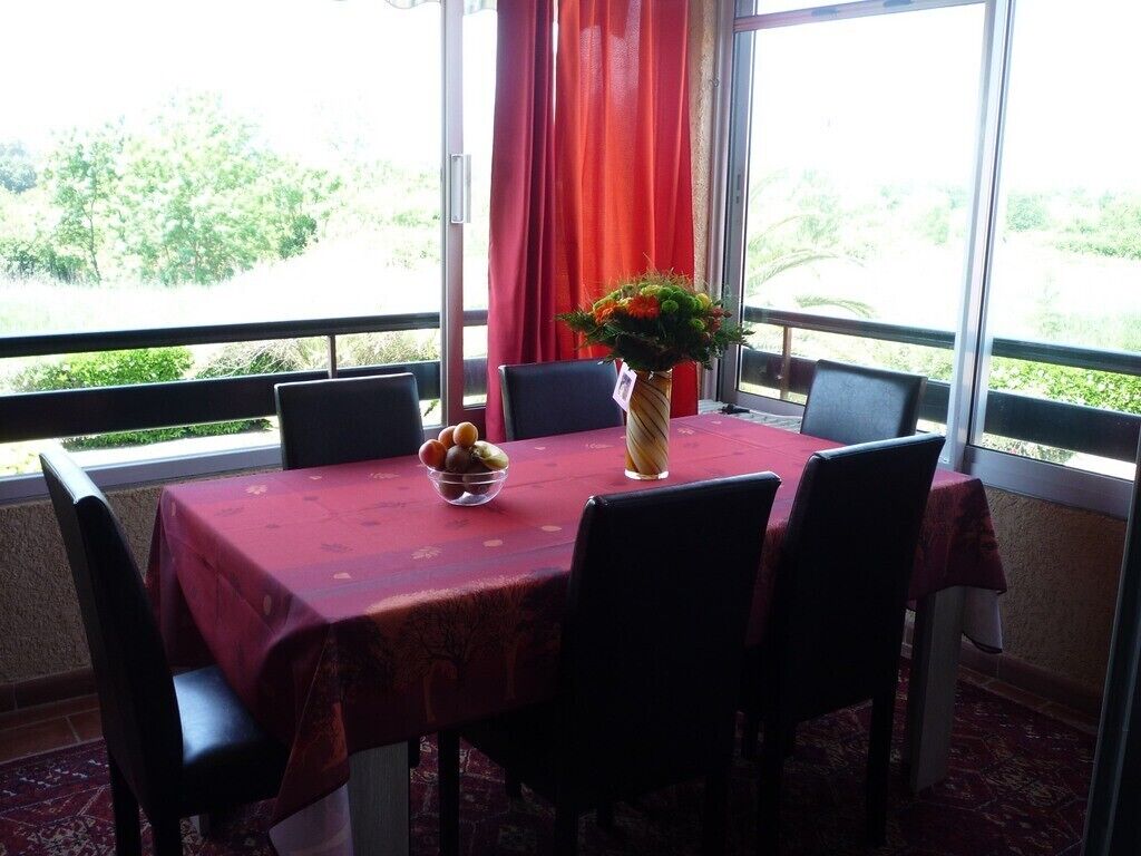 Ein Esstisch mit rotem Tischläufer, umgeben von Stühlen, und eine Vase mit Blumen.