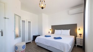 A modern hotel room with a large bed, bedside lamps, a mirror, a small stool, and an air conditioning unit. - Elvin Bozcaada (Bozcaada)