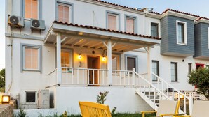 A two-story house with a balcony, a staircase, and outdoor seating. - Elvin Bozcaada (Bozcaada)