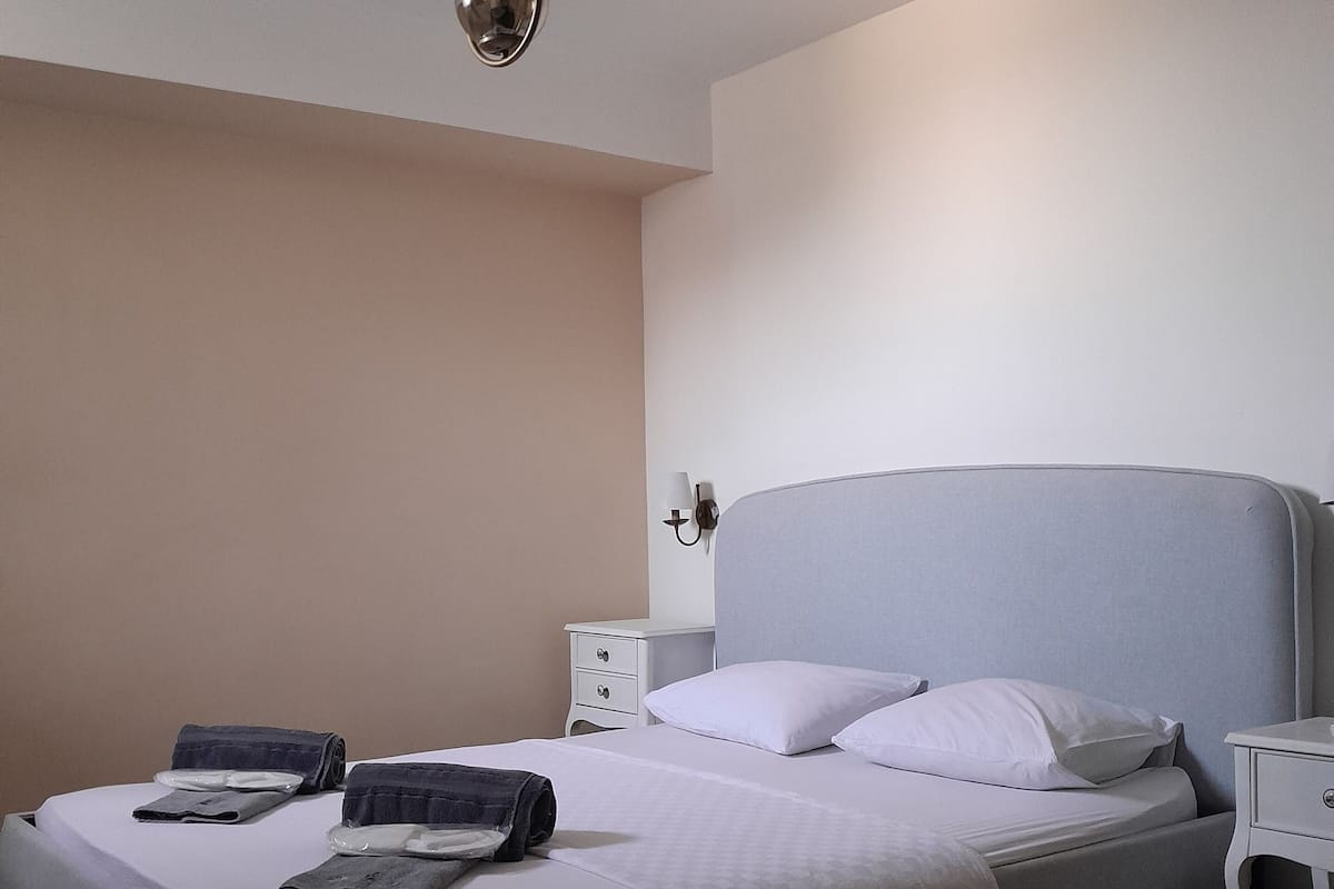 A neatly made bed with pillows and folded towels, a bedside table with a lamp, and a nightstand with a lamp.