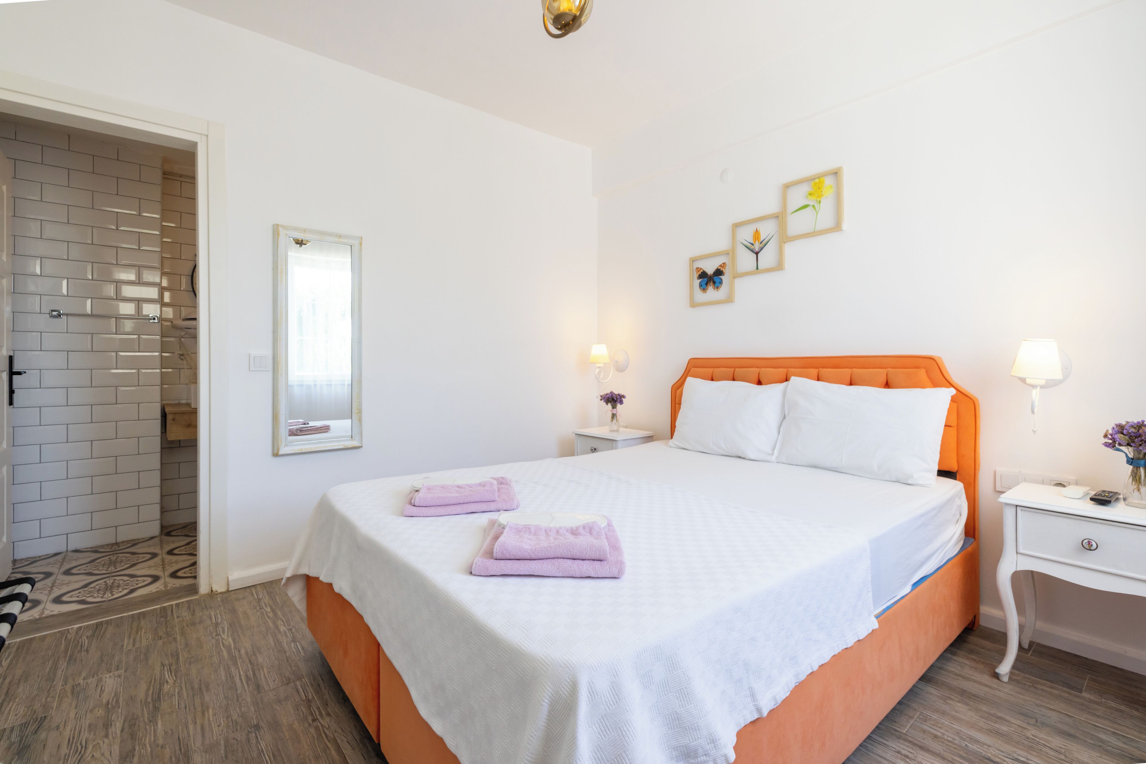 A neatly arranged bedroom with a bed, two bedside tables, a nightstand, a mirror, and a door leading to a bathroom.